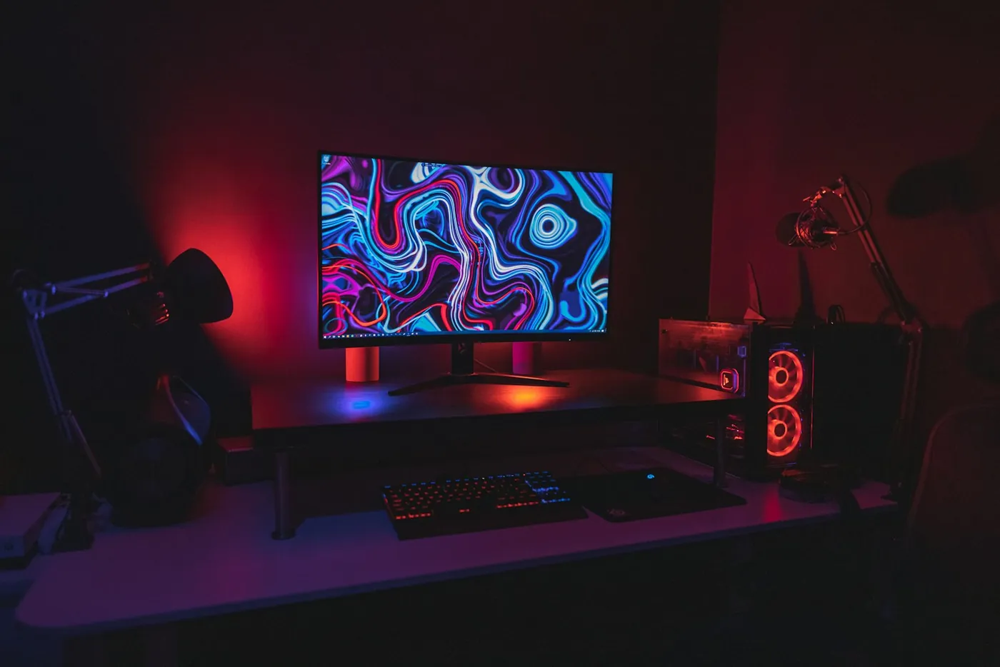 Streaming desk with a microphone on a boom arm, a headset and a PC tower in red light